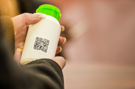 Close up of a woman s hand showing an empty plastic flask with QR code information in a blurred backgroundの写真素材