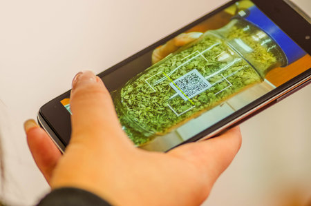 Close up of woman s hand scanning voucher code qr with mobile phone to a flask of marjoram, in a...