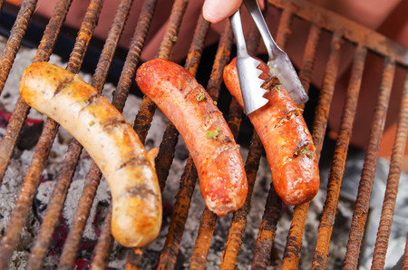 Close up of woman s hand holding a tongs turning the grilling sausages on barbecue grill. BBQ. Bavarian sausagesの写真素材