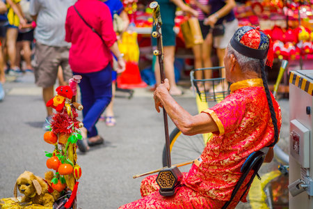 SINGAPORE, SINGAPORE - FEBRUARY 01, 2018: Elder street musician busking along a busy street during...