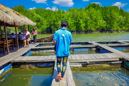 AO NANG, THAILAND - FEBRUARY 19, 2018: Outdoor view of unidentified man walking at farm fish wood restaurant sea river with small pools at Krabi Thailandのeditorial素材