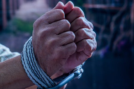 Close up of man hands wrapped with rope around wrists in captivity , victim abused, slave of work, respect for human rights and exploitation concept isolated on blurred backgroundの写真素材