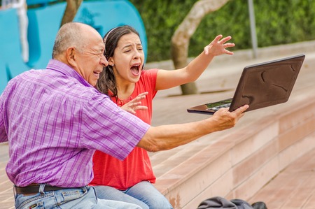 Outdoor view of father holding and computer and sacry daugher screaming afraid of his dad throw the computer in the ground, at parkの写真素材