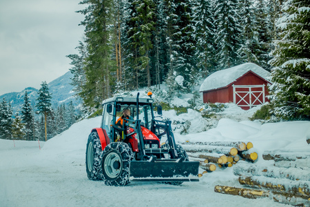 Valdres, Norway - March 26, 2018: Outdoor view of unidentified man in a small truck working, moving the trunks in the snow close to a wooden house covered with snow in Norwayのeditorial素材