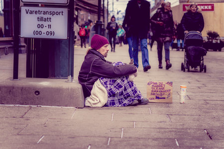 OSLO, NORWAY - MARCH, 26, 2018: Outdoor view of unidentified homeless man sitting in the ground asking for money in the streets of Oslo townのeditorial素材