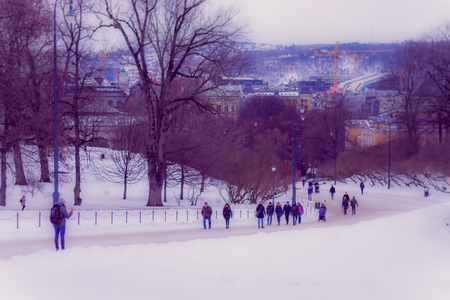 OSLO, NORWAY - MARCH, 26, 2018: Outdoor view of unidentified people walking in the streets surrounding of trees covered with snow in Oslo townのeditorial素材