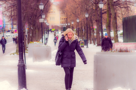 OSLO, NORWAY - MARCH, 26, 2018: Outdoor view of beautiful blonde woman using her cellphone and walking in a public park in Oslanのeditorial素材