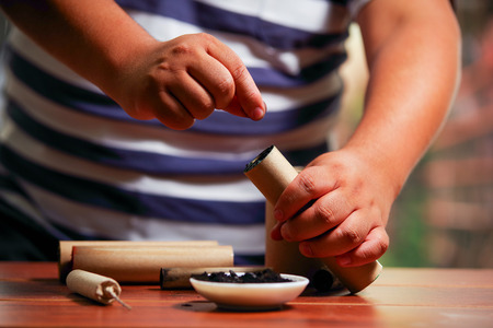 Close up of man preparing brown firecracker close to bowl with gunpowder, over a wooden tableの写真素材