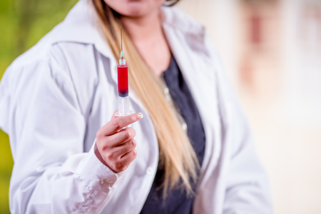 Close up of woman wearing a lab coat and holding a syringe with blood in her handの写真素材