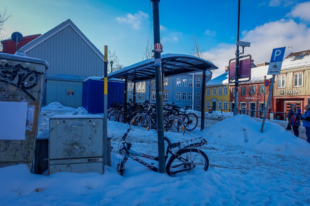TRONDHEIM, NORWAY - APRIL 04, 2018: Unidentified people in the streets and row of bikes under a bus stop close to traditional Scandinavian wooden houses stand along the street in Trondheimのeditorial素材