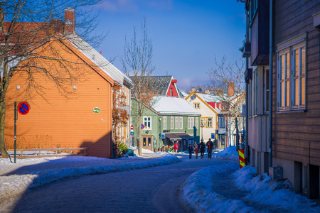 TRONDHEIM, NORWAY - APRIL 04, 2018: Outdoor view of unidentified people walking in a small and old street close to Scandinavian wooden buildings stand along old street in Trondheim, Norwayのeditorial素材