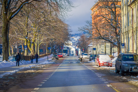 TRONDHEIM, NORWAY - APRIL 04, 2018: Outdoor view of unidentified people walking in a sidewalk close to some cars parked in the streets in traditional Scandinavian buildings in Trondheimのeditorial素材