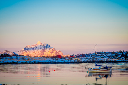 SVOLVAER, LOFOTEN ISLANDS, NORWAY - APRIL 10, 2018: Outdoor view with a partial frozen lake with a boat sailing close to the coastのeditorial素材