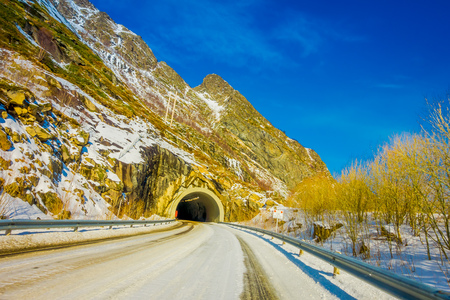 LOFOTEN, NORWAY, APRIL, 10, 2018: View of frozen street with an informative sign at the enter of a tunnel in Skjelfjord in Lofoten Islandsのeditorial素材