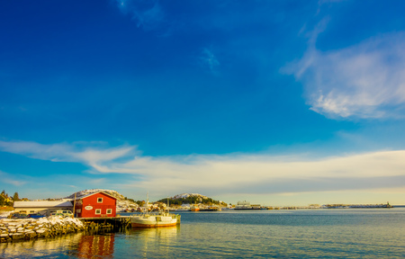 Henningsvaer, Norway - April 04, 2018: Outdoor view of wooden building in the bay with boat at shore in Lofoten Islands durring a gorgeous sunny dayのeditorial素材