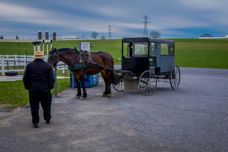 Pennsylvania, USA, APRIL, 18, 2018: Outdoor view of unidentified man walking close to a parked Amish buggy carriage in a farm with a horse used for a pull the car in the streetsのeditorial素材