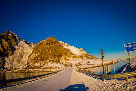 Henningsvaer, Norway - April 04, 2018: Outdoor view of frozen street covered with snow and traffic lights an informative signs during a sunny dayのeditorial素材