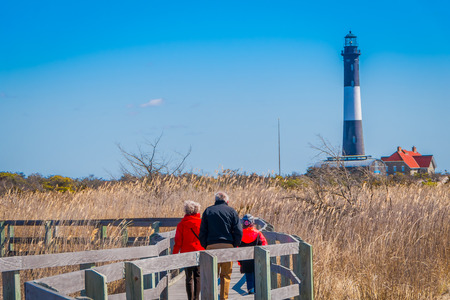 LONG ISLAND, USA, APRIL, 04, 2018: Outdoor view of unidentified people walking in a long wooden bridge in a beautiful sunny day with blue sky with Montauk Lighthouse behind, at Long islandのeditorial素材
