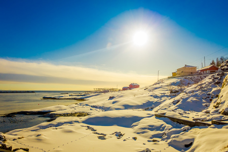 Outdoor view of some buildings in the bay of Lofoten Islands surrounded with snowy mountains and colorful winter station and sun shinny in the skyの写真素材