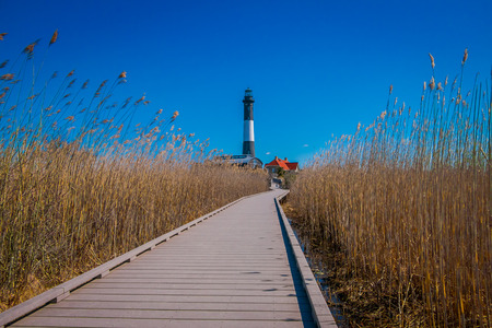 LONG ISLAND, USA, APRIL, 04, 2018: Outdoor view of long wooden bridge in a beautiful sunny day with blue sky with Montauk Lighthouse behind, at Long islandのeditorial素材