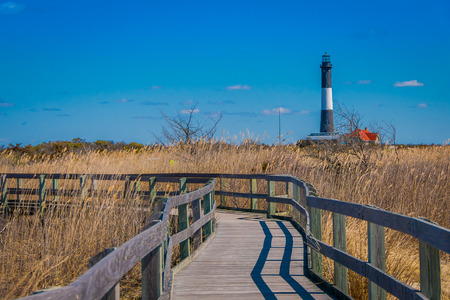 LONG ISLAND, USA, APRIL, 04, 2018: Outdoor view of long wooden bridge in a beautiful sunny day with gorgeous blue sky with Montauk Lighthouse behind, at Long islandのeditorial素材