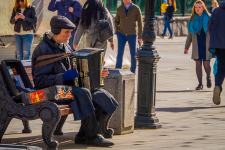 MOSCOW, RUSSIA- APRIL, 24, 2018: Outdoor view of unidentified man sitting in a public chair and playing the accordion on Nikolskaya street in gorgeous sunny dayのeditorial素材