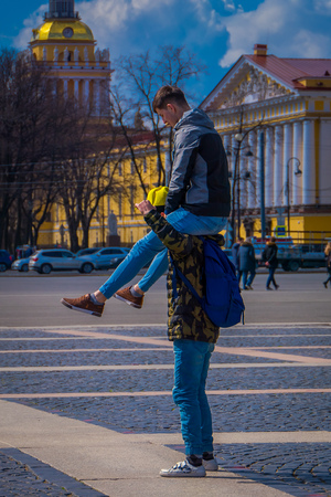 ST. PETERSBURG, RUSSIA, 02 MAY 2018: Unidentified man over the shoulders of his friend or boyfriend doing acrobatics with the Admiralty building behind, during a sunny day in st. Petersburgのeditorial素材
