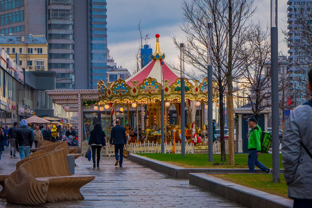 MOSCOW, RUSSIA- APRIL, 24, 2018: Outdoor view of unidentified people walking in a park close to a carousel horses in a Red Square with some buildings behind in Moscowのeditorial素材