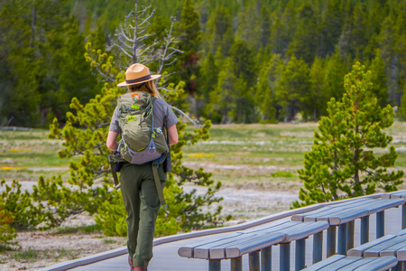 YELLOWSTONE, MONTANA, USA MAY 24, 2018: Outdoor view of female park ranger wearing a green uniform with a backpack, walking along the wooden path in the Old Faithful Upper Geyser Basinのeditorial素材