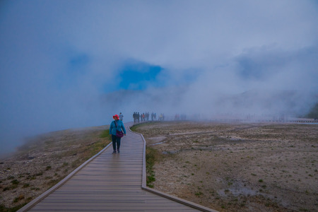 YELLOWSTONE, MONTANA, USA MAY 24, 2018: Tourists walk around the Grand Prismatic Spring in Yellowstone National park on a boardwalk surrounded by vapor. This geyser is one of the most activeのeditorial素材