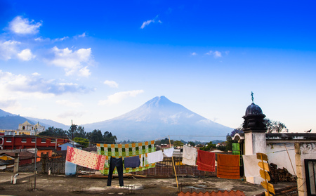 Volcano Agua above the roofs of old quarters of Antigua in a beautiful sunny day and blue sky in the city of Antigua Guatemala.の写真素材