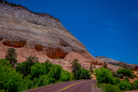 Beautiful view of red asphalt scenic road among the picturesque mountains of orange and red sandstone in a gorgeous sunny day and blue sky in Zion National Park in USA.の写真素材