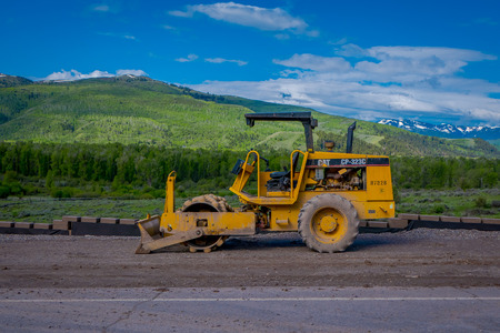YELLOWSTONE NATIONAL PARK, WYOMING, USA - JUNE 07, 2018: Road construction equipment parked in a construction zone. Roadwork in Yellowstone National Park in gorgeous sunny day and blue sky backgroundのeditorial素材