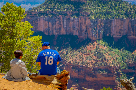 Grand Canyon,Arizona USA, JUNE, 14, 2018: Outdoor view of father and son sitting in the ground close to the border and enjoying the landscape of bright Angel canyon, in Arizonaのeditorial素材