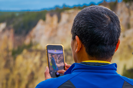 YELLOWSTONE NATIONAL PARK, WYOMING, USA - JUNE 07, 2018: Close up of selective focus of man using a cellphone to take a picture of a friend in Yellowstone Falls in Yellowstone National Parkのeditorial素材