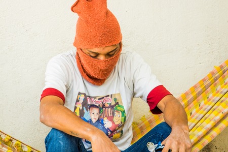 QUITO, ECUADOR, AUGUST 21, 2018: Close up of unidentified man sitting in a hammock and wearing a orange hood covering his face and head, inside of a refuge centerのeditorial素材