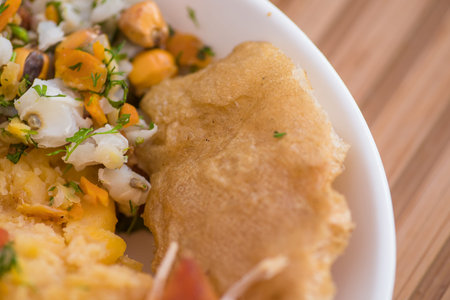 Close up of small pieces of roasted pork skin served with mashed potatoes, salad, tostado, mote...