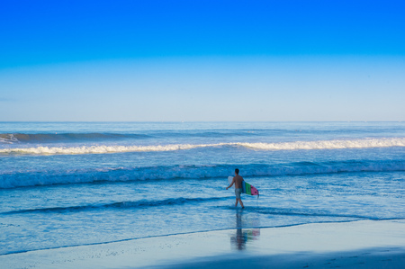 Santa Teresa, Costa Rica - June, 28, 2018: Young teen walking in the shore of the beach of Santa Teresa with his surfboard ready to surf in a beautiful sunny day with blue sky and blue waterのeditorial素材