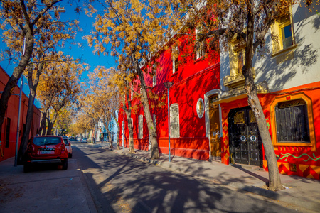 SANTIAGO, CHILE - SEPTEMBER 13, 2018: Cars parked under trees at one side of the street in the Barrio Yungay with red building wall in Santiagoのeditorial素材