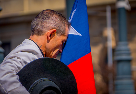 SANTIAGO, CHILE - SEPTEMBER 13, 2018: Unidentified man wearing white t-shirt and holding a black hat in his hand while he kiss a chilean flag in Armas square in Santiagoのeditorial素材