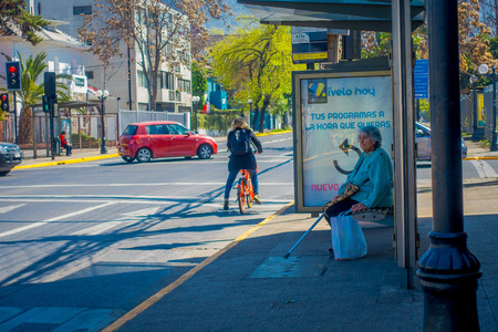 SANTIAGO, CHILE - SEPTEMBER 13, 2018: Unidentified woman waiting the bus in a busstop with some people riding a bike in downtown street of the city of Santiagoのeditorial素材