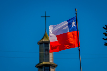 Exterior detail view of chilean flag waving with a blurred vilupulli church behind, wooden churches located at Chiloe island, Chileの写真素材