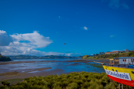 CHILOE, CHILE - SEPTEMBER, 27, 2018: View of beautiful colorful wooden restaurant cebiche on stilts palafitos, in a low tide day wooden house of yellow and red color at sunny day in Castro, Chiloe Islandのeditorial素材