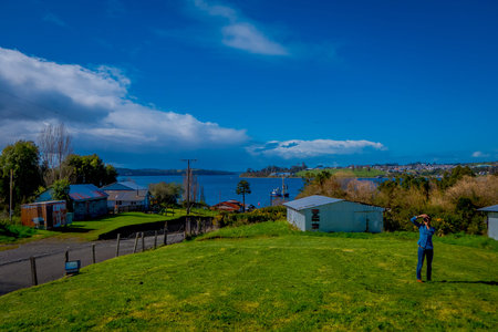 CHILOE, CHILE - SEPTEMBER, 27, 2018: Outdoor view of landscape with a woman taking pictures and posing with house buildings in the horizont just right behind her Chiloe islandのeditorial素材