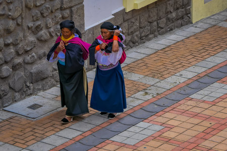 COTACACHI, ECUADOR, NOVEMBER 06, 2018: Outdoor view of two indigenous woman walking together in the streets of Cotacachi and holding in their back bags of clothes in the city of Cotacachiのeditorial素材