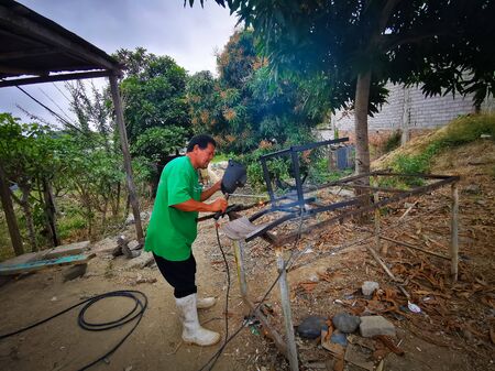 Same, ECUADOR, 10 October 2019: Unidentified welder on a side road, welding together two pieces of metal, chairのeditorial素材