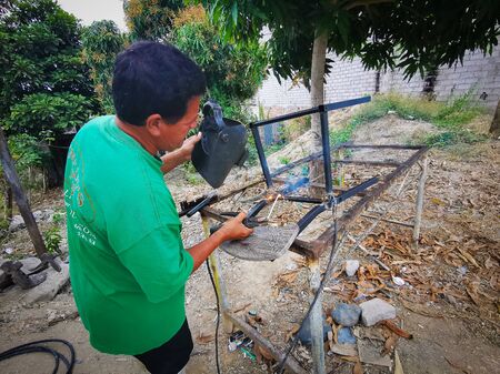 Same, ECUADOR, 10 October 2019: Unidentified welder on a side road, welding together two pieces of metal, chairのeditorial素材