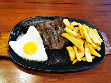 Healthy fried egg french fries and meat steak on plate, wood background.の写真素材