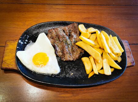 Healthy fried egg french fries and meat steak on plate, wood background.の写真素材