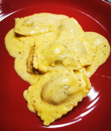 Raviolli. Cooked raviolli on a shiny red plate, 4 cheese sauce.の写真素材